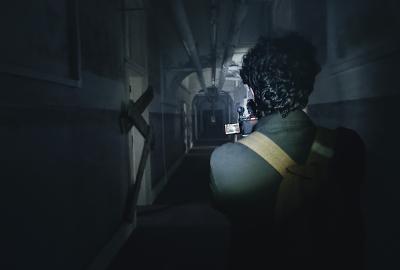 Adam holding a camera and torch down a dark eerie hallway.  
