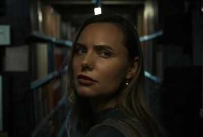 “A new visitor looks over her shoulder while finding her way through the library’s dark back-stacks.”