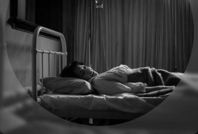 A young woman lies in bed in an asylum