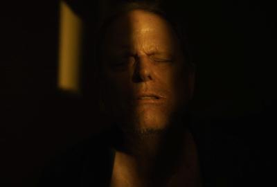 A man with his eyes shut sits in the shadows