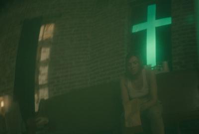 Woman sits in a church with a neon cross