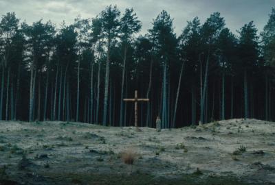 A woman walks towards the woods with a large cross planted in the ground