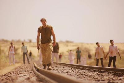 The Dead 2, India! man walks on railroad tracks with zombies in the background