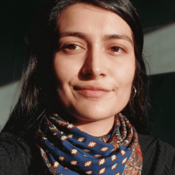 A mixed-race woman in her thirties with black hair stares intently at the camera, smiling slightly