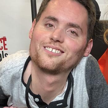 A mid 30s man in a wheelchair smiling at the camera.
