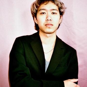 Headshot portrait of Joel Nasan Roberson, Thai-American Filmmaker against a pink backdrop