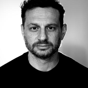 A front facing headshot in black and white of director Nick Psinakis.