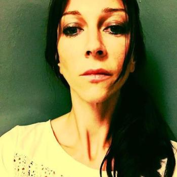 A woman with dark hair stares head on into the camera